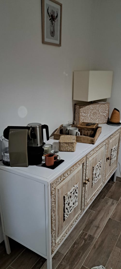 Armoire blanchie à la chaux avec détails sculptés ornementaux accueillant une cafetière et paniers de rangement aux Loyes B&B, Jaillans