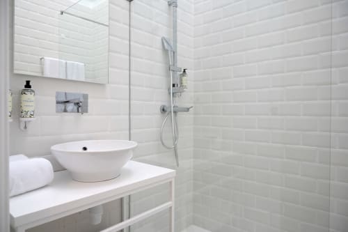 Banheiro moderno no hotel Oporto Comfort Charming no Porto com azulejos brancos tipo metrô, pia redonda tipo vessel, chuveiro walk-in e