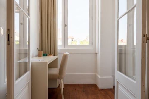 Espaço de trabalho luminoso em quarto de hotel no Porto com secretária, cadeira e vista para jardim através de grandes janelas