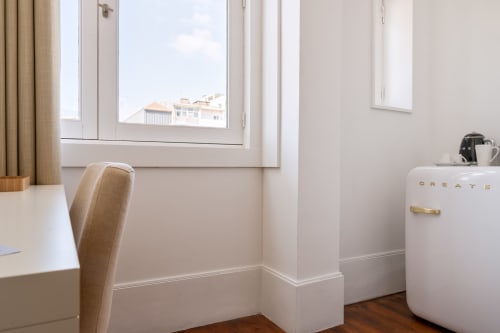 Quarto moderno do Oporto Comfort Charming Cedofeita no Porto com secretária, cadeira bege, frigorífico branco e vista para o jardim