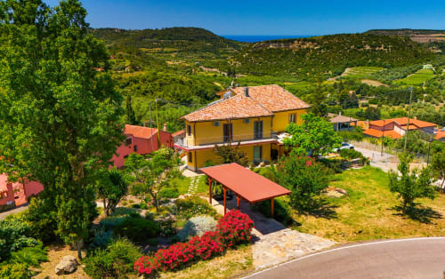 Villa gialla con tetto rosso a Modolo, Sardegna, circondata da paesaggio verde e giardini mediterranei