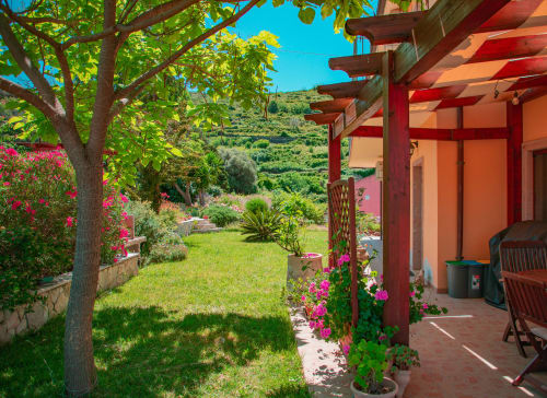 Terrazza della villa Sardegna Explora House con pergola rossa, fiori in fiore, vista sul giardino e dolci colline a Modolo