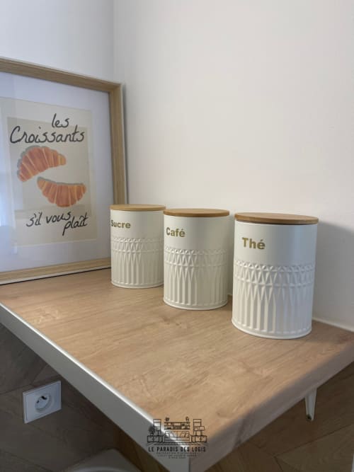 Comptoir de cuisine avec trois bacs de rangement étiquetés et affiche de croissants à Le Paradis Des Logis