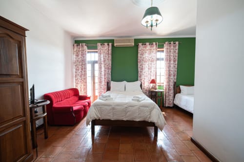 Suíte familiar Casa Augusta em Penafiel com paredes verdes, sofá vermelho, cama de casal e cortinas florais rosa nas janelas