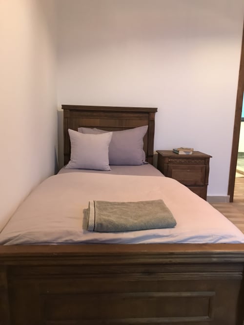 Cozy bedroom at Imsouane Surf Paradise with wooden bed, purple pillows, folded towel, and nightstand in Agadir, Morocco