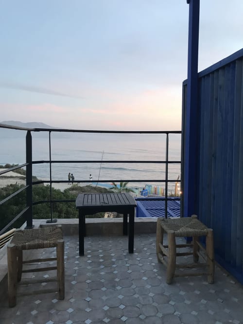 Tiguemi room terrace at Imsouane Surf Paradise with sea view, woven stools, and sunset over the coast