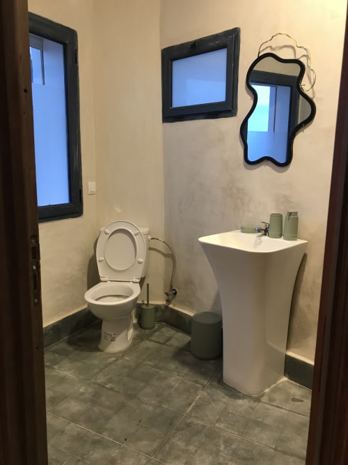 Modern bathroom at Imsouane Surf Paradise hotel with toilet, pedestal sink, mirrors, and sea-view window in Agadir, Morocco