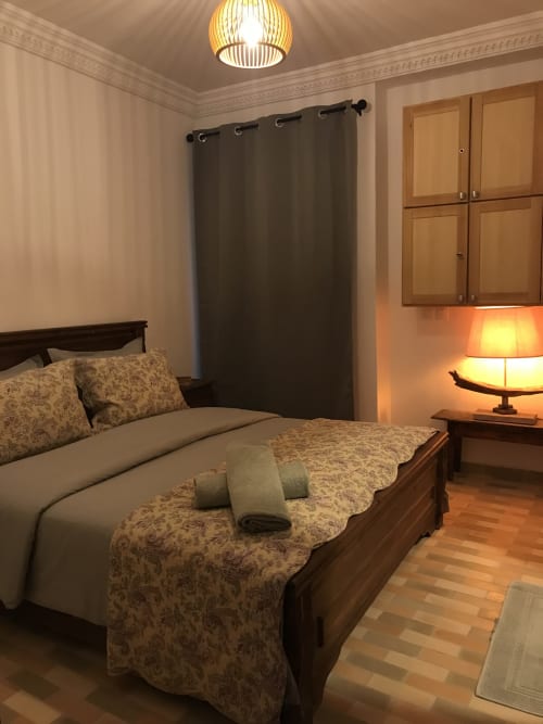 Elegant bedroom at Imsouane Surf Paradise with wooden bed, patterned bedding, ambient lighting, and dark curtains