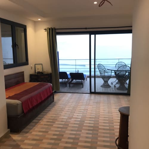 Spacious bedroom at Imsouane Surf Paradise with sea view balcony, bed with red throw, and wicker chairs overlooking ocean