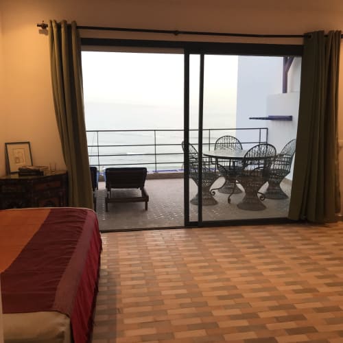 Bedroom with sea view terrace at Imsouane Surf Paradise, featuring glass doors opening to balcony with wicker chairs