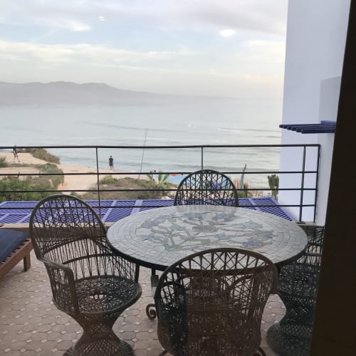 Beachfront terrace with wicker chairs at Imsouane Surf Paradise, Morocco, overlooking sea and mountains
