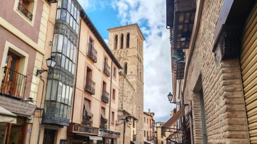 Calle medieval de Toledo con edificios históricos y torre de iglesia cerca del hotel Príncipe David