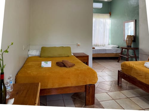 Habitación del hostal Cayuco Maya en Bacalar con cama de madera, colcha dorada, acentos verdes y aire acondicionado