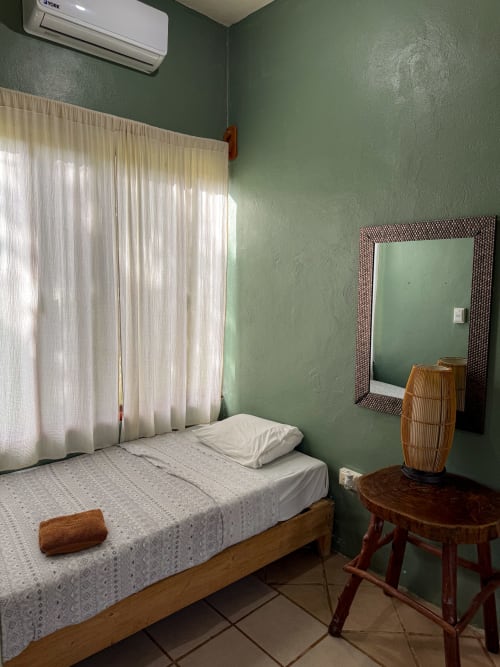 Habitación del hostal Cayuco Maya en Bacalar con paredes verdes, cama de madera y cortinas translúcidas