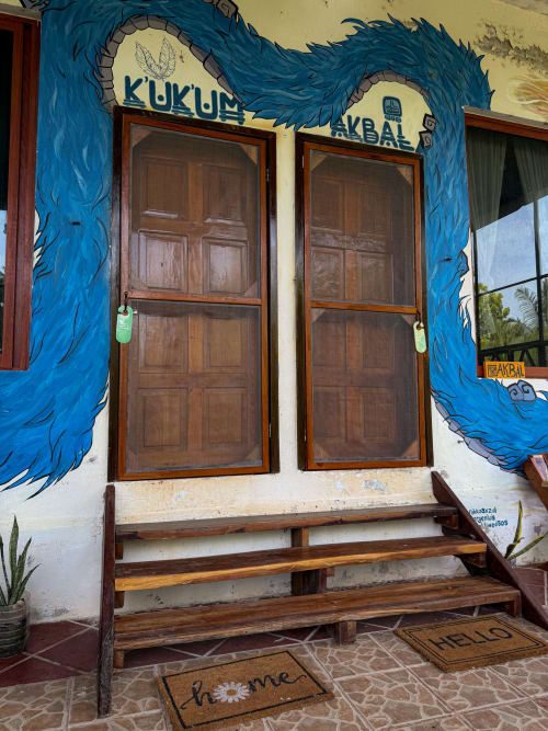 Mural de dragón azul colorido enmarca las puertas de madera en la entrada del hostal Cayuco Maya en Bacalar