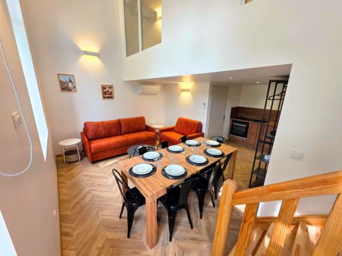 Modern open-plan dining area at Vindihouses with wooden table, orange sofa, and kitchen in Epinac