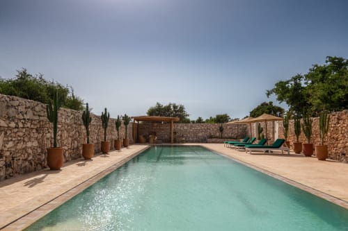 Piscine turquoise entourée de murs en pierre et de cactus au Domaine Belhazar, retraite luxe à Essaouira