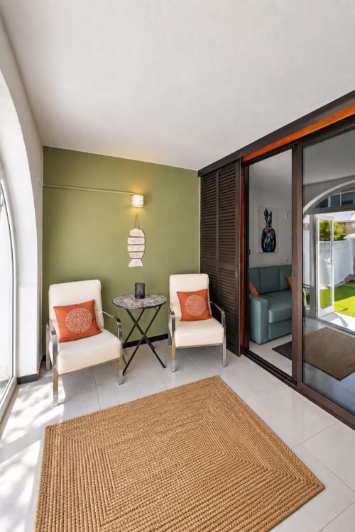 Modern patio seating area with olive green wall, cream chairs with orange pillows, and glass doors at Manage Home Tenerife