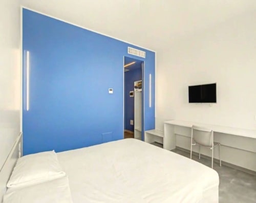 Moderna camera d'hotel a Ca'Tron a Dolo con parete di accento blu, letto bianco, scrivania e TV a schermo piatto
