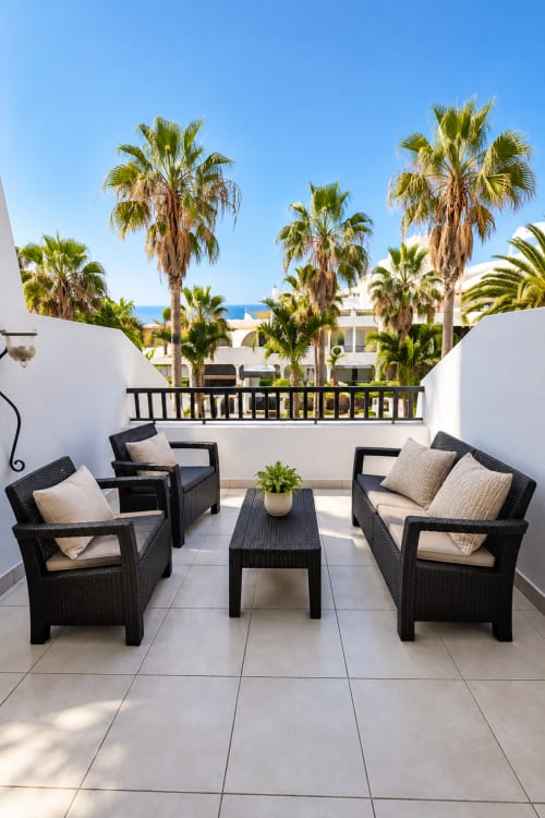 Modern terrace with black wicker chairs overlooking palm trees and Mediterranean architecture in Playa de las Américas,