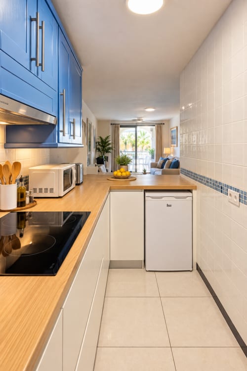 Modern kitchen with blue cabinets, wooden counters, and open-plan living area in Playa de las Américas apartment