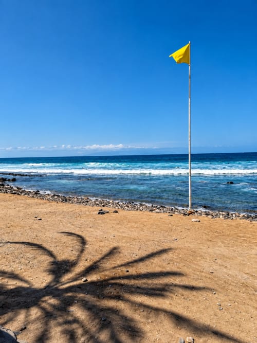 Yellow flag on Playa de las Américas beach with waves and clear blue sky in Tenerife