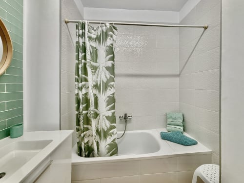 Modern bathroom with white subway tile, green leaf shower curtain, and bathtub in Manage Home Tenerife apartment, Los