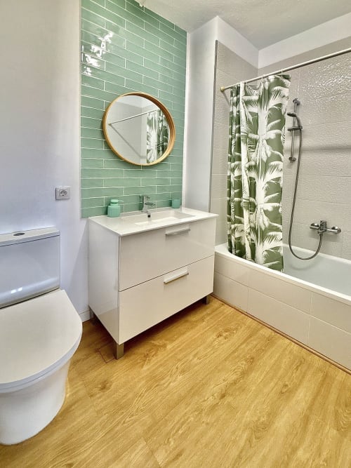 Modern bathroom in Manage Home Tenerife apartment with green subway tile, wooden vanity, round mirror, and tropical shower