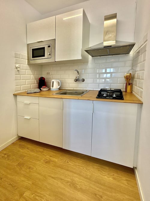 Modern white kitchen with wooden counters, gas stove, and microwave in Los Cristianos apartment