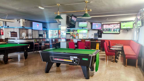 Sports bar lounge with pool tables, red seating, and multiple TV screens at Manage Home Tenerife apartment in Los Cristianos