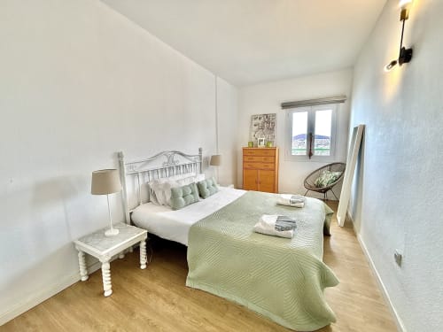 Modern bedroom in Los Cristianos apartment with sea view, white metal bed, green bedding, wooden furniture, and natural light
