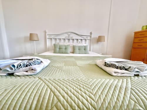 Bright bedroom at Manage Home Tenerife with white metal headboard, green bedspread, and side lamps in Los Cristianos