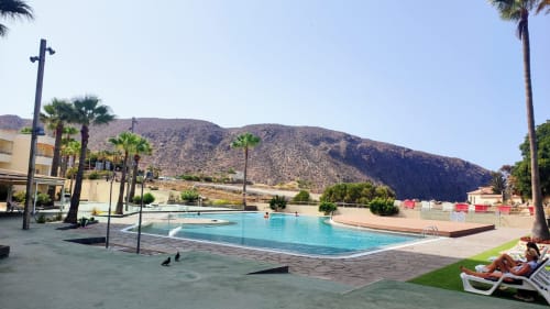 Resort pool with turquoise water, palm trees, and mountain backdrop in Los Cristianos, Tenerife