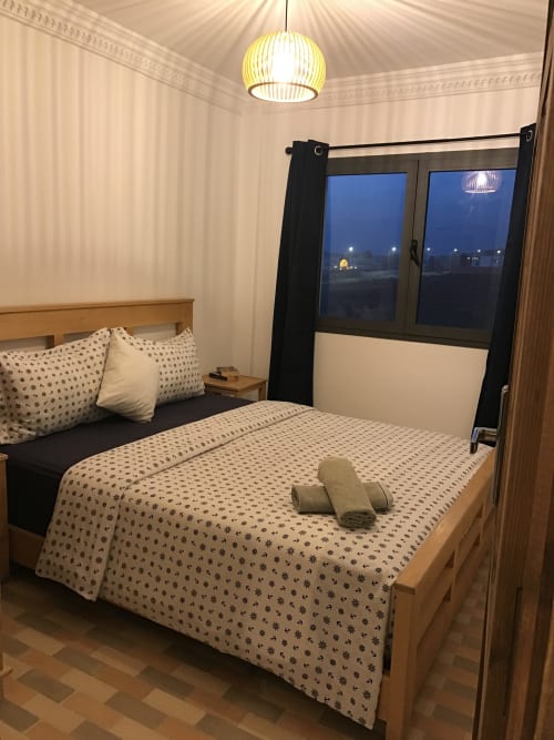 Modern bedroom at Imsouane Surf Paradise with wooden bed, patterned bedding, pendant light, and sea view through black