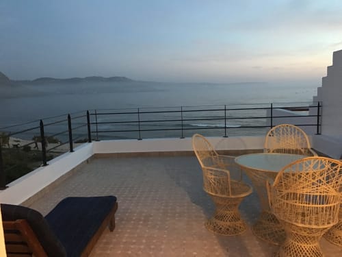 Sunset terrace view at Imsouane Surf Paradise with wicker chairs, sea views, and coastal mountains in Agadir, Morocco