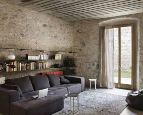 Modern living room in Alemanys 5 cottage, Girona with dark sofa, exposed stone walls, built-in shelving, and glass doors