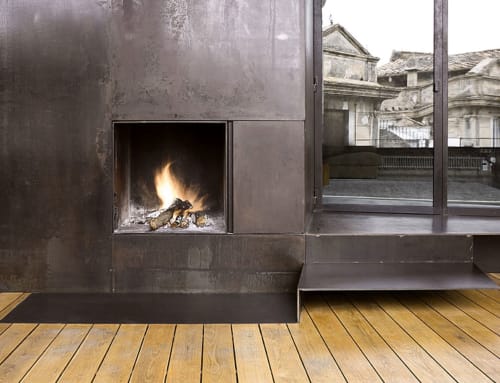 Modern fireplace in Alemanys 5 cottage, Girona with metal surround, wood deck, and city views through glass doors