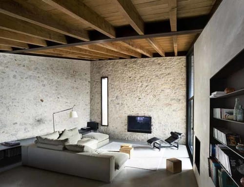 Modern cottage living room at Alemanys 5 in Girona with stone walls, wooden beams, white sofa, TV, and shelving