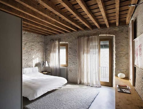 Spacious bedroom at Alemanys 5 in Girona with exposed wooden beams, stone walls, and modern furnishings