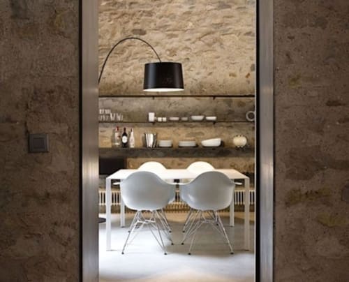Modern dining area at Alemanys 5 Girona with white chairs, stone walls, arc lamp, and open shelving displaying decor