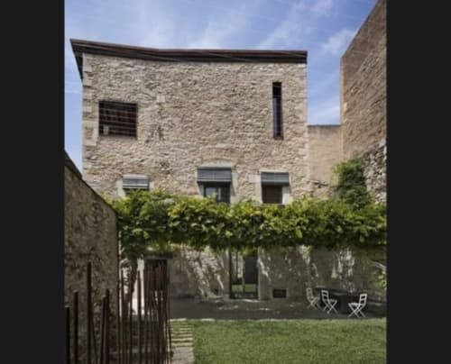 Alemanys 5 courtyard in Girona with stone walls, lawn, dining chairs, and ivy-covered trellis
