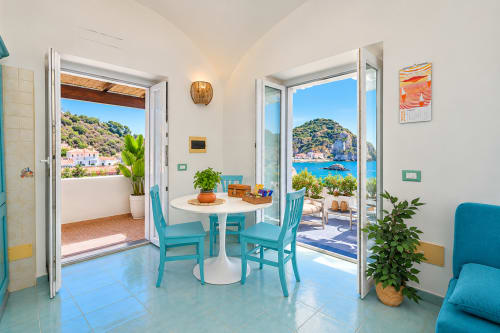 Luminosa zona pranzo mediterranea a Sant'Angelo con sedie turchesi, terrazza con vista mare affacciata sulle scogliere costiere