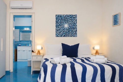 Modern bedroom at Chiaia di Rose with blue-striped bedding, navy pillow, and en-suite bathroom visible through doorway in