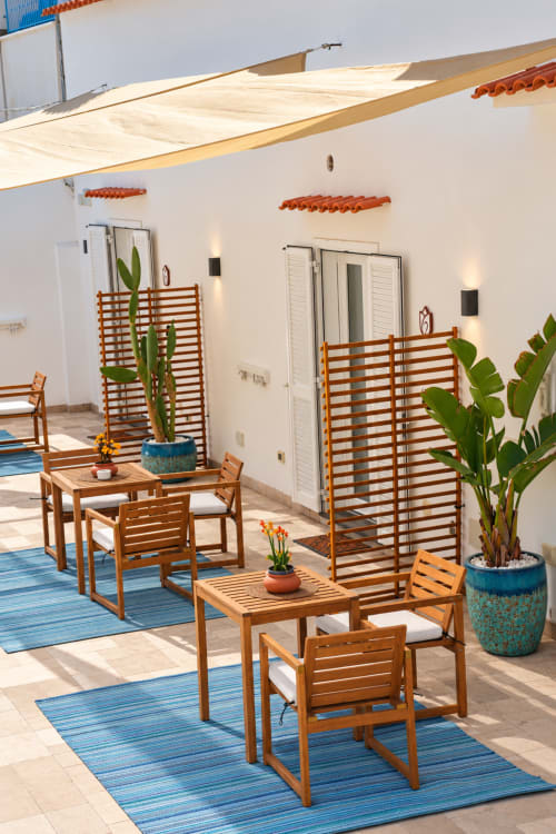 Sunny terrace at Chiaia di Rose B&B with wooden furniture, potted plants, and blue striped rugs in Serrara Fontana, Italy.