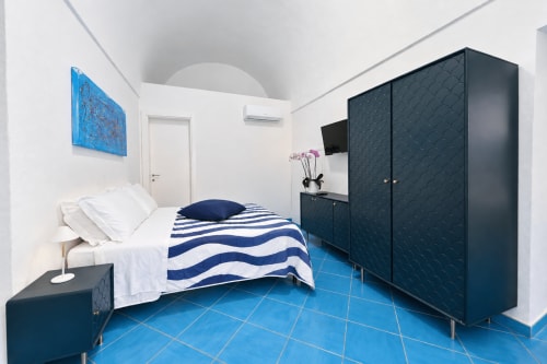 Camera da letto moderna con pavimento in piastrelle blu, biancheria a righe blu scuro, arredamenti scuri e pareti bianche al Chiaia di Rose B&B a Serrara