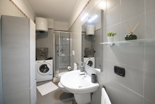 Bagno moderno dell'hotel di Ferrara con lavabo su piedistallo bianco, doccia e unità lavatrice-asciugatrice integrate