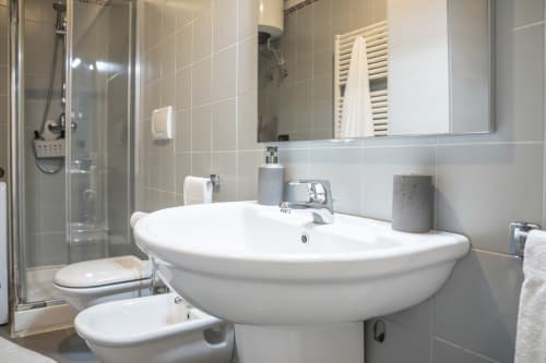 Bagno moderno con lavabo a piedistallo bianco, toilette, doccia e specchio nell'appartamento LikeHome CRILU a Ferrara, Italia