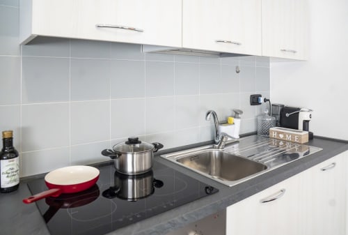 Cucina moderna con piano lavoro nero, lavello in acciaio inossidabile, pentola rossa e rivestimento in piastrelle bianche nell'appartamento di Ferrara