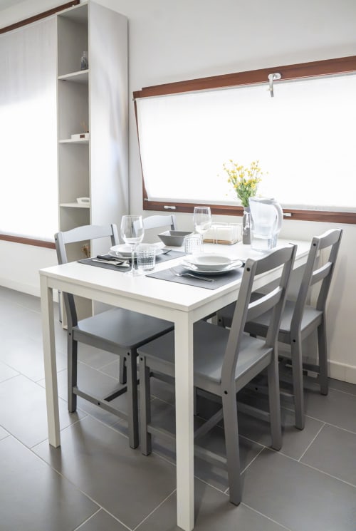 Moderna zona pranzo con tavolo bianco, sedie grigie e fiori gialli nella camera d'hotel a Ferrara