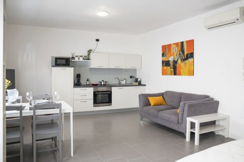 Moderno monolocale a Ferrara con cucina aperta, zona living, divano grigio e opere d'arte astratta colorata